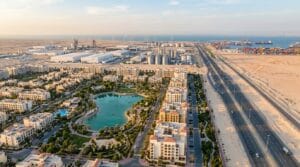 منظر جوي لمحور القاهرة–الإسماعيلية–السويس: مجتمع سكني حديث في المقدمة وطريق صحراوي واسع يمتد نحو مناطق صناعية وميناء عند الأفق